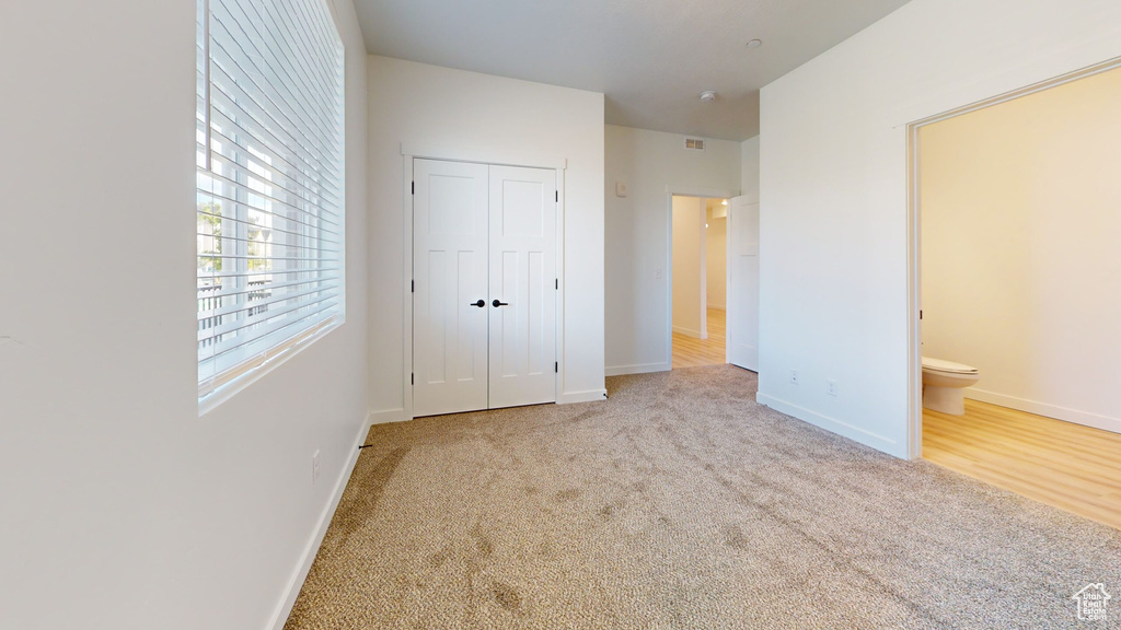 Unfurnished bedroom with connected bathroom, light hardwood / wood-style floors, and a closet