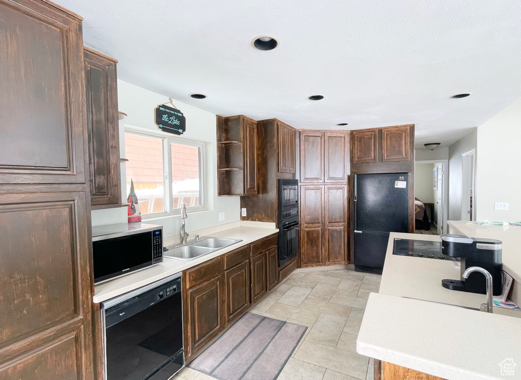 Kitchen featuring light tile flooring, black appliances, dark brown cabinets, and sink