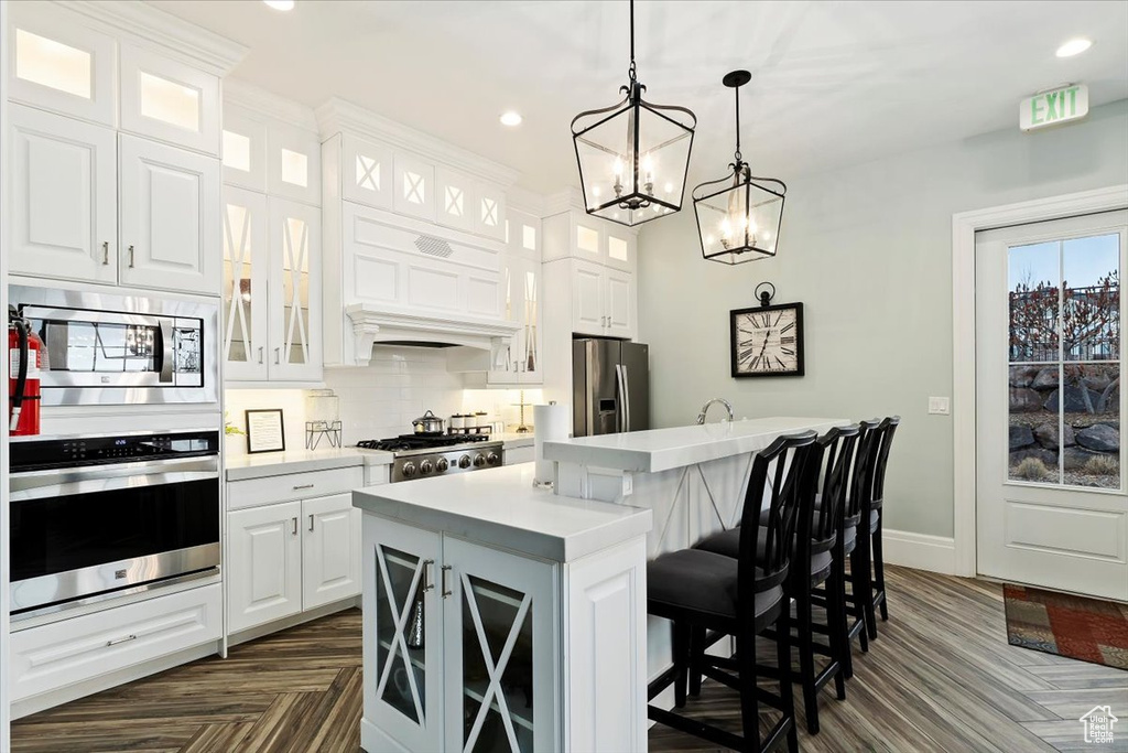 Kitchen with white cabinetry, a kitchen island, a breakfast bar, appliances with stainless steel finishes, and dark parquet flooring