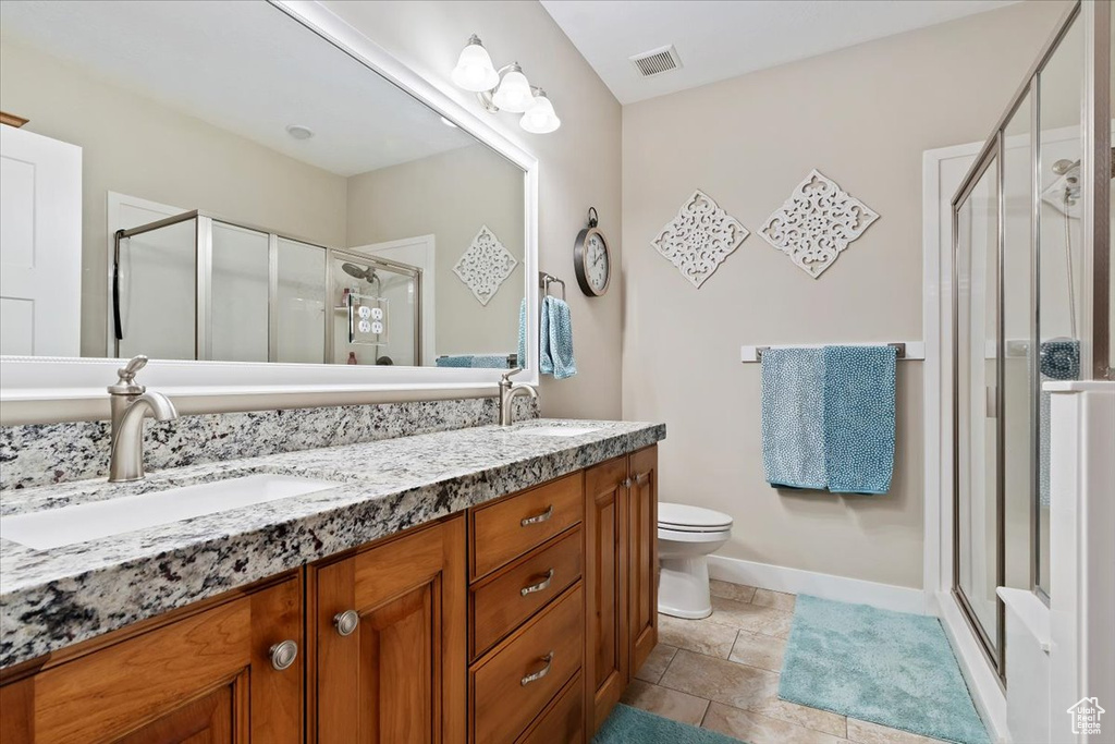 Bathroom with an enclosed shower, toilet, tile flooring, double sink, and vanity with extensive cabinet space