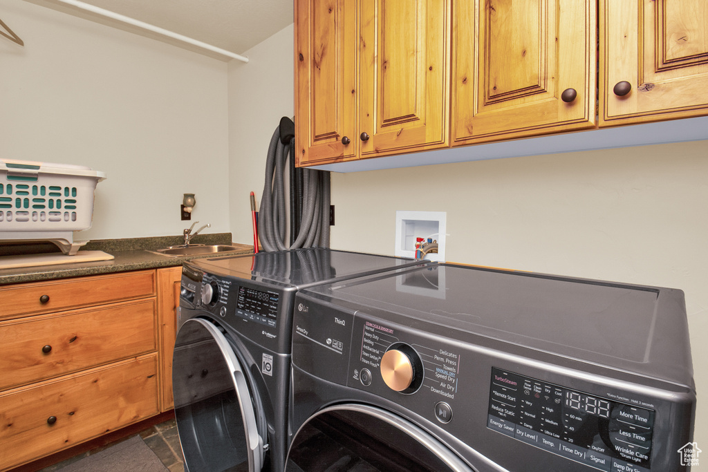 Clothes washing area with washer and dryer, cabinets, sink, and dark tile floors