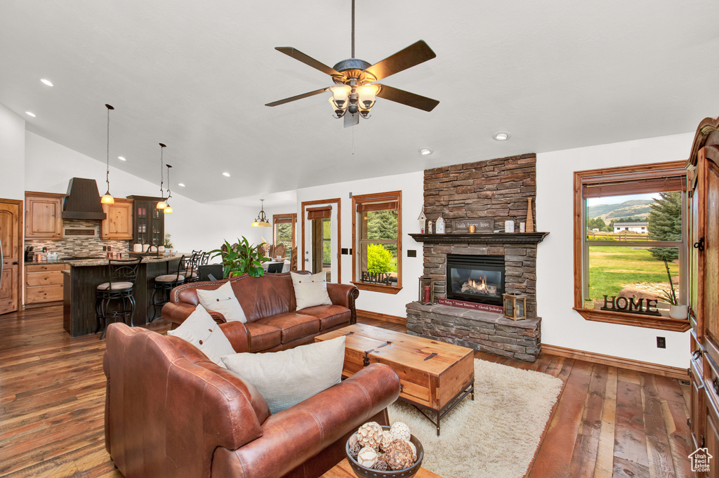 Living room featuring a fireplace, ceiling fan, vaulted ceiling, and dark wood-type flooring
