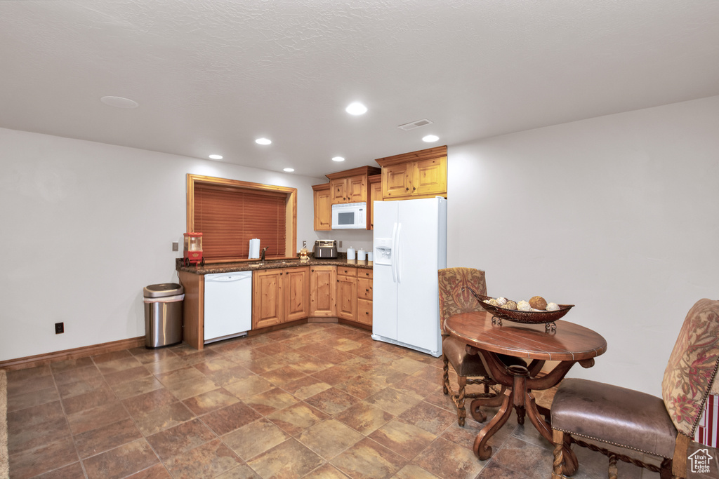 Kitchen featuring light brown cabinets, dark stone countertops, dark tile flooring, white appliances, and sink