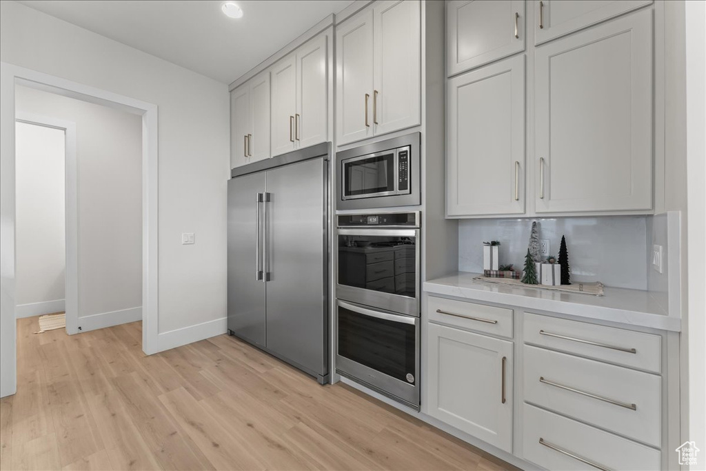 Kitchen with white cabinets, light hardwood / wood-style flooring, and built in appliances