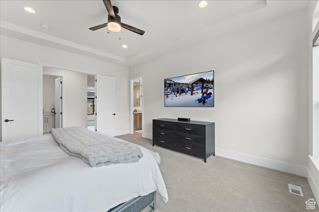 Carpeted bedroom with connected bathroom, a raised ceiling, and ceiling fan