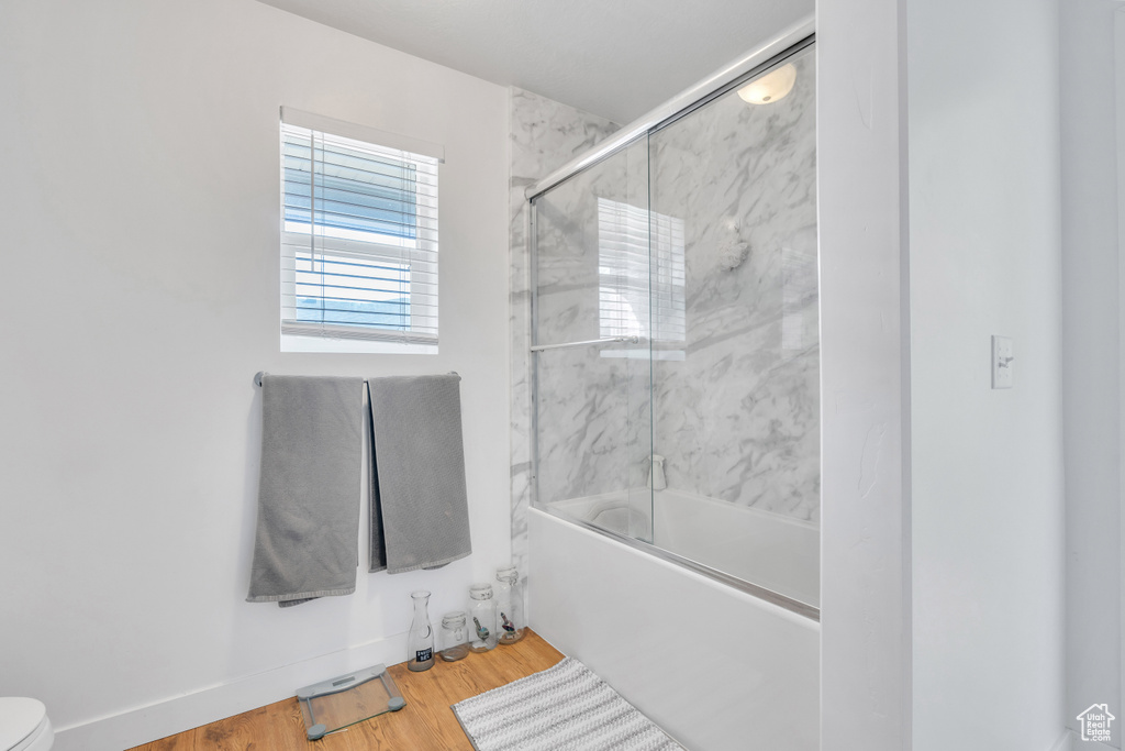 Bathroom with bath / shower combo with glass door, hardwood / wood-style flooring, and toilet