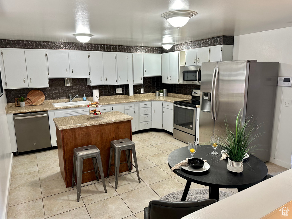 Kitchen featuring backsplash, stainless steel appliances, white cabinetry, a center island, and light stone countertops