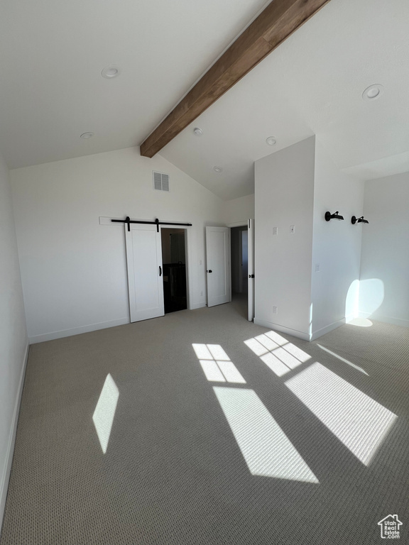 Spare room with vaulted ceiling with beams, light colored carpet, and a barn door