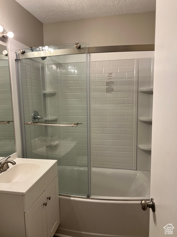Bathroom with enclosed tub / shower combo, a textured ceiling, and vanity with extensive cabinet space