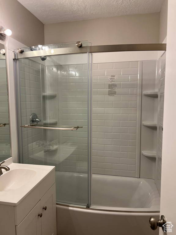 Bathroom with vanity, shower / bath combination with glass door, and a textured ceiling