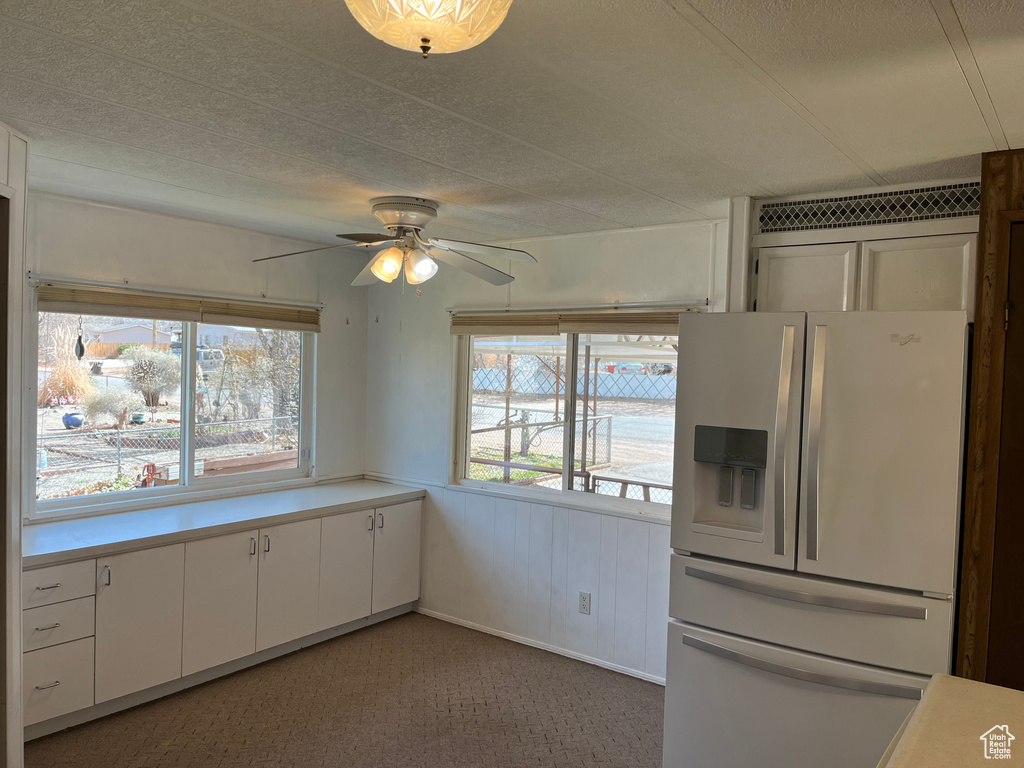 Kitchen featuring white cabinets, white fridge with ice dispenser, ceiling fan, and carpet flooring
