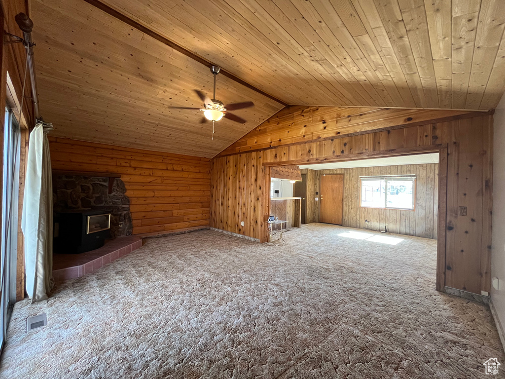 Carpeted spare room with a stone fireplace, ceiling fan, wood ceiling, and lofted ceiling