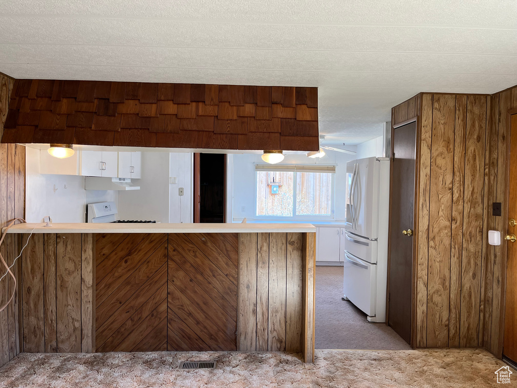Kitchen with carpet flooring, wood walls, stove, white refrigerator, and kitchen peninsula