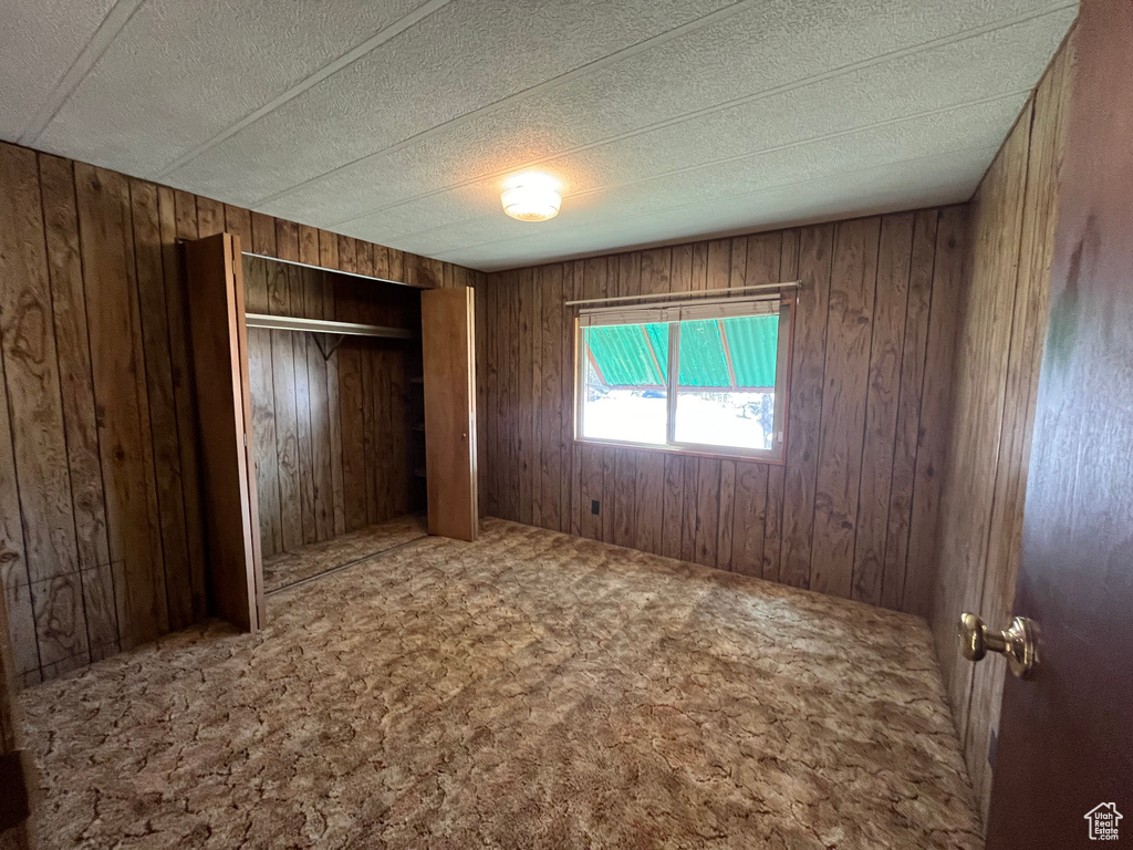 Unfurnished bedroom featuring a closet, wooden walls, a textured ceiling, and carpet
