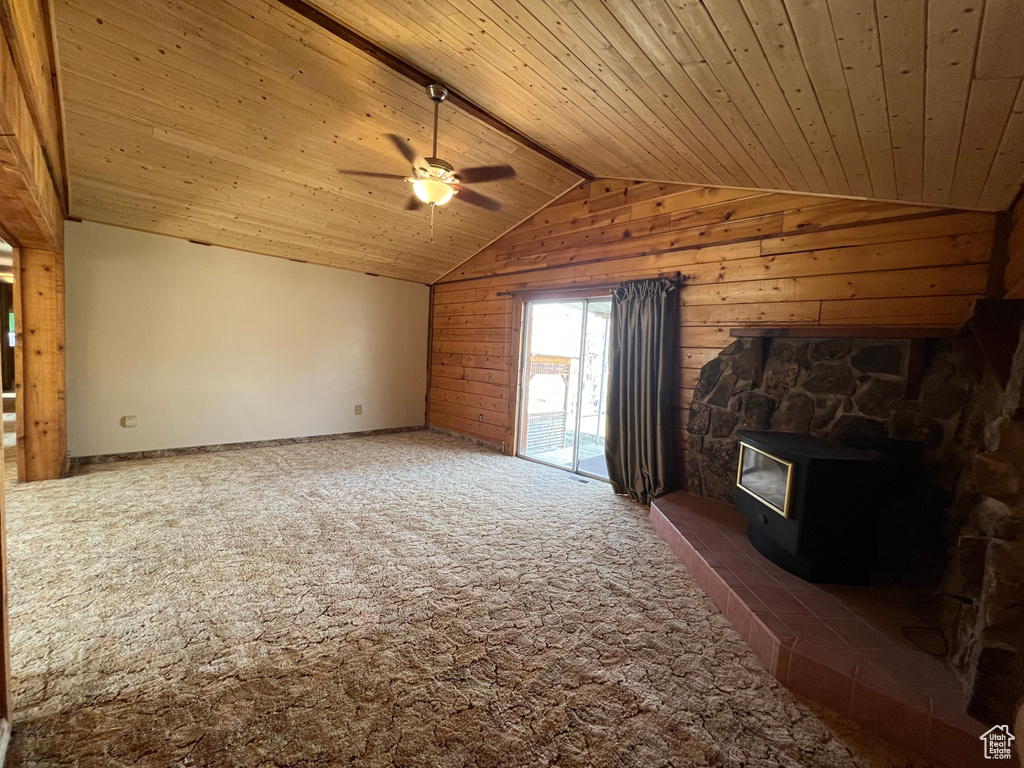 Unfurnished living room with dark carpet, a wood stove, wood ceiling, vaulted ceiling, and ceiling fan