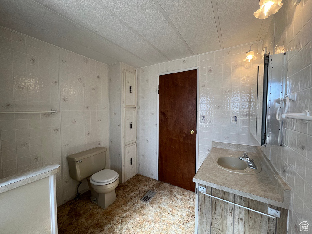 Bathroom with vanity, toilet, tile walls, and a textured ceiling