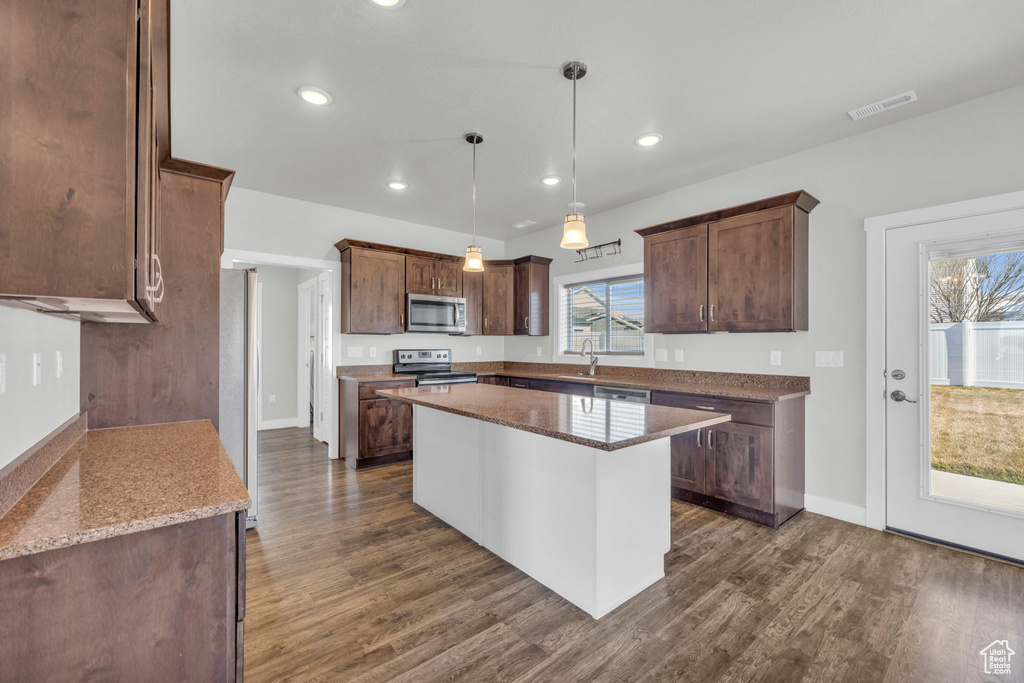 Kitchen featuring pendant lighting, dark wood-type flooring, a center island, light stone counters, and stainless steel appliances
