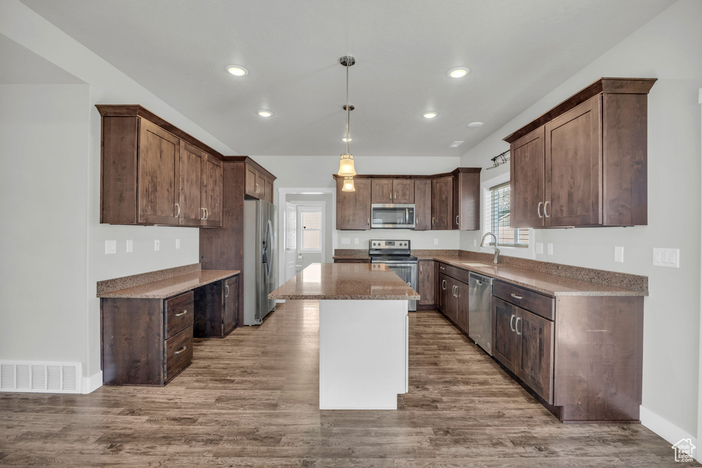 Kitchen with sink, appliances with stainless steel finishes, decorative light fixtures, a center island, and light hardwood / wood-style floors