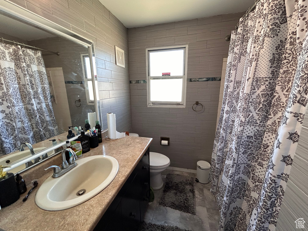 Bathroom featuring toilet, tile walls, tile floors, and oversized vanity