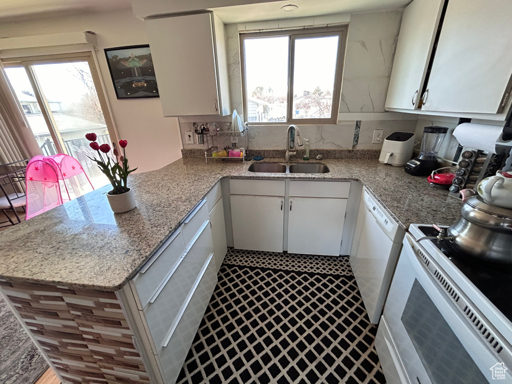 Kitchen featuring light stone counters, white cabinetry, backsplash, kitchen peninsula, and sink