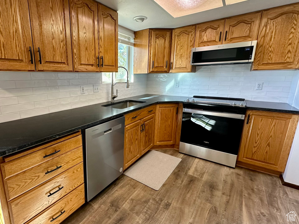 Kitchen featuring light hardwood / wood-style floors, tasteful backsplash, sink, dark stone countertops, and appliances with stainless steel finishes