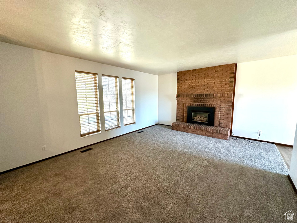Unfurnished living room with a fireplace, brick wall, and carpet floors