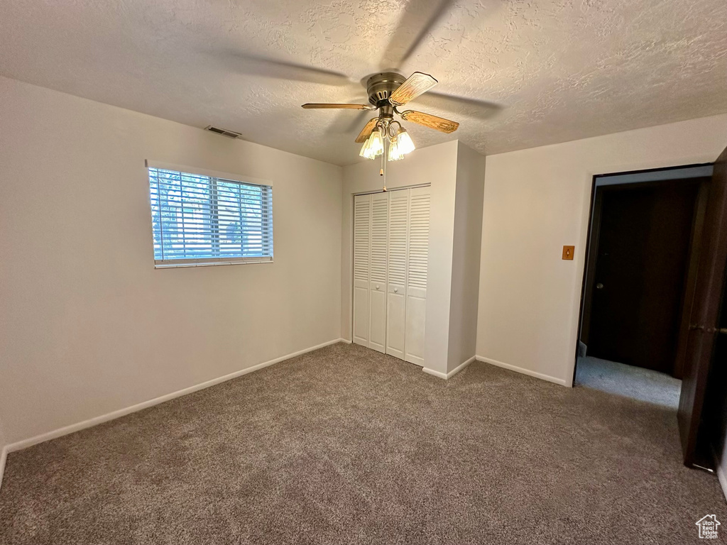 Unfurnished bedroom with dark colored carpet, ceiling fan, a textured ceiling, and a closet
