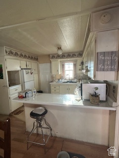 Kitchen with white cabinets, hardwood / wood-style flooring, kitchen peninsula, a kitchen breakfast bar, and white refrigerator