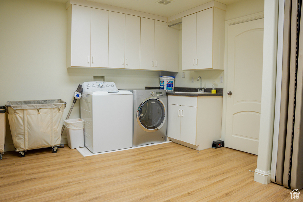 Laundry room with cabinets, sink, washing machine and clothes dryer, and light wood-type flooring