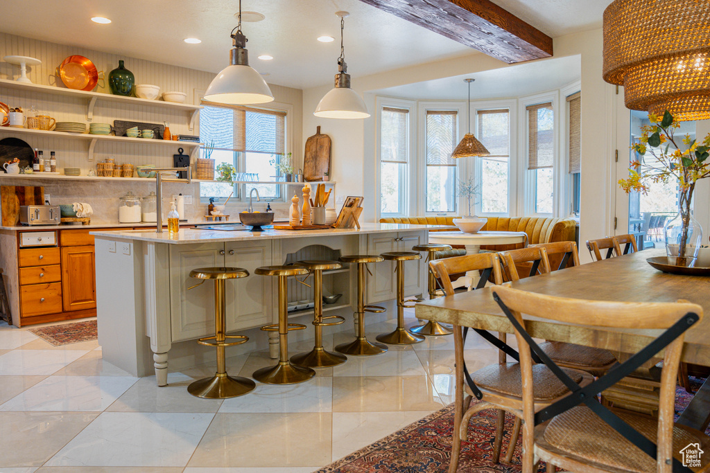 Kitchen featuring light tile flooring, hanging light fixtures, a kitchen breakfast bar, and beam ceiling