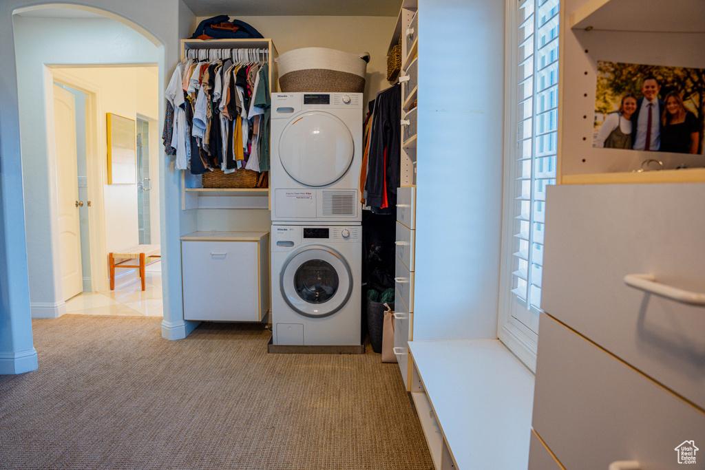 Clothes washing area featuring light colored carpet and stacked washer / drying machine