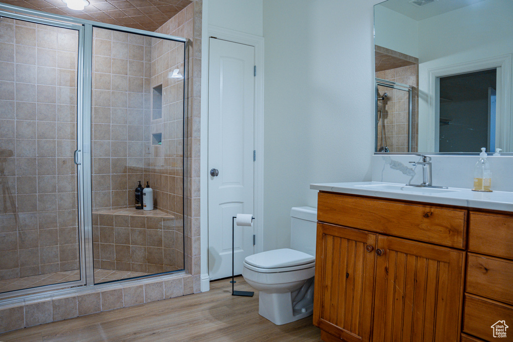 Bathroom featuring wood-type flooring, large vanity, walk in shower, and toilet