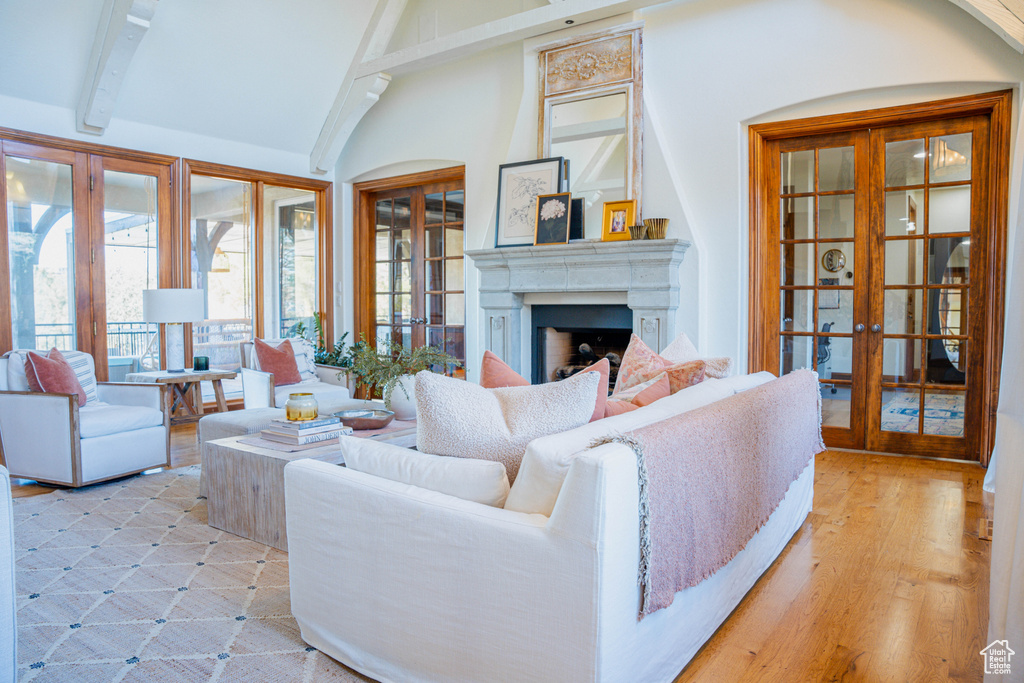 Living room featuring light wood-type flooring, beam ceiling, high vaulted ceiling, and french doors