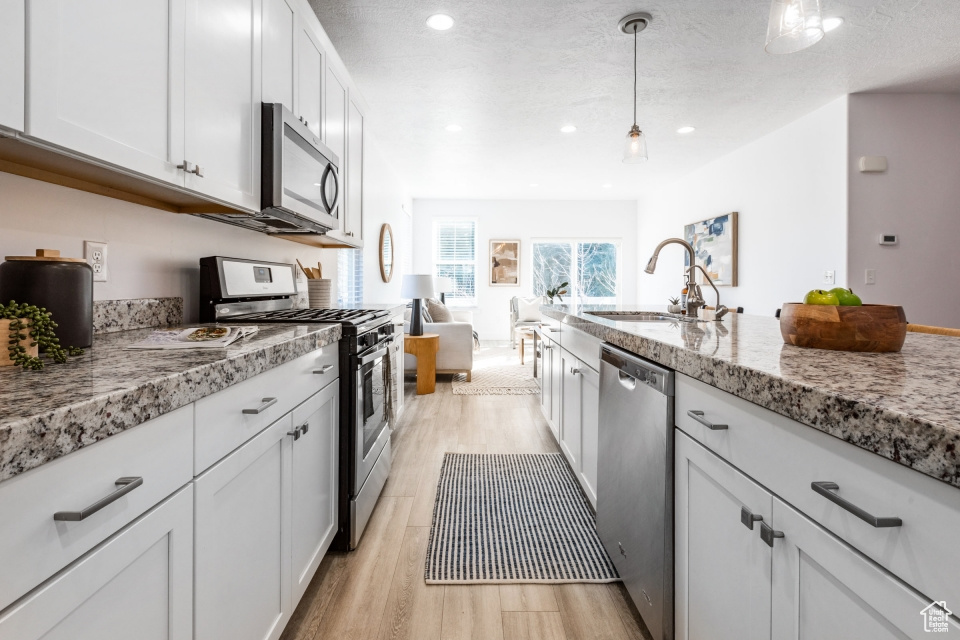 Kitchen featuring light stone counters, white cabinets, hanging light fixtures, appliances with stainless steel finishes, and light hardwood / wood-style flooring