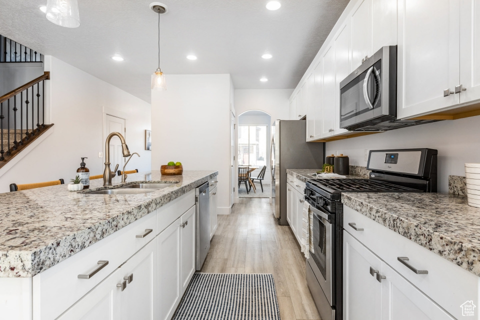 Kitchen with white cabinetry, appliances with stainless steel finishes, light hardwood / wood-style floors, sink, and decorative light fixtures