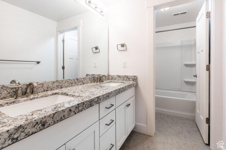 Bathroom featuring dual vanity, shower / tub combination, and tile floors