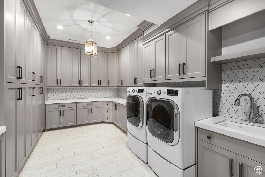 Laundry area with sink, washing machine and clothes dryer, light tile floors, and cabinets