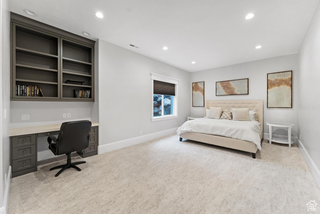 Bedroom with light colored carpet and built in desk