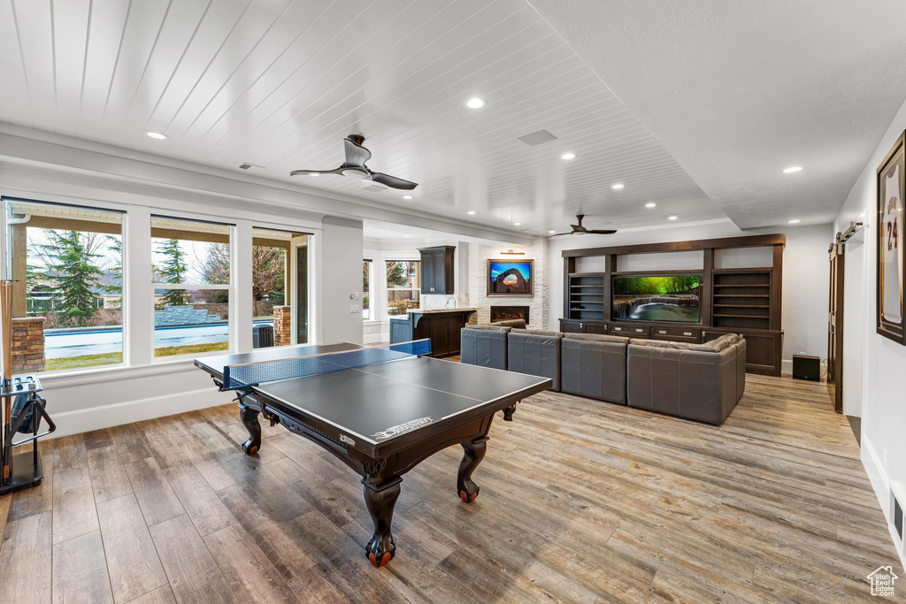 Rec room featuring light hardwood / wood-style floors, ceiling fan, and a large fireplace