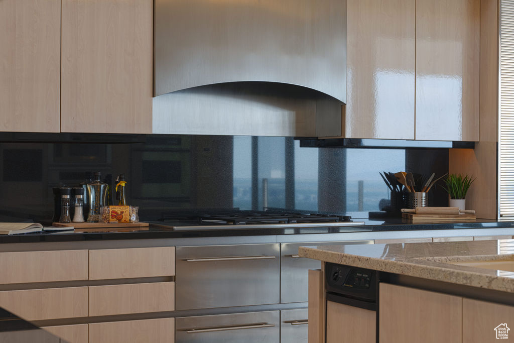 Kitchen featuring stainless steel gas cooktop, dark stone counters, ventilation hood, light brown cabinetry, and a wealth of natural light