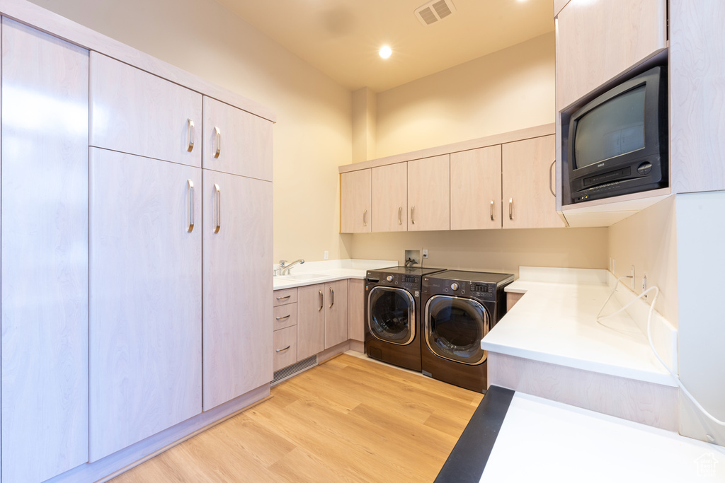 Clothes washing area featuring light hardwood / wood-style floors, sink, hookup for a washing machine, and washing machine and clothes dryer