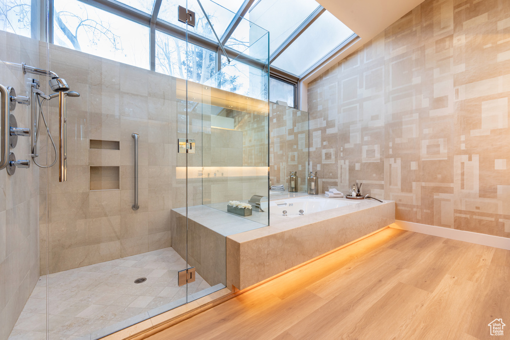 Bathroom with hardwood / wood-style floors, independent shower and bath, and lofted ceiling with skylight