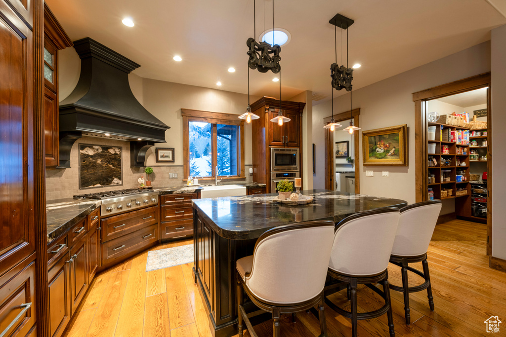 Kitchen with light hardwood / wood-style floors, a kitchen breakfast bar, a kitchen island, and custom range hood
