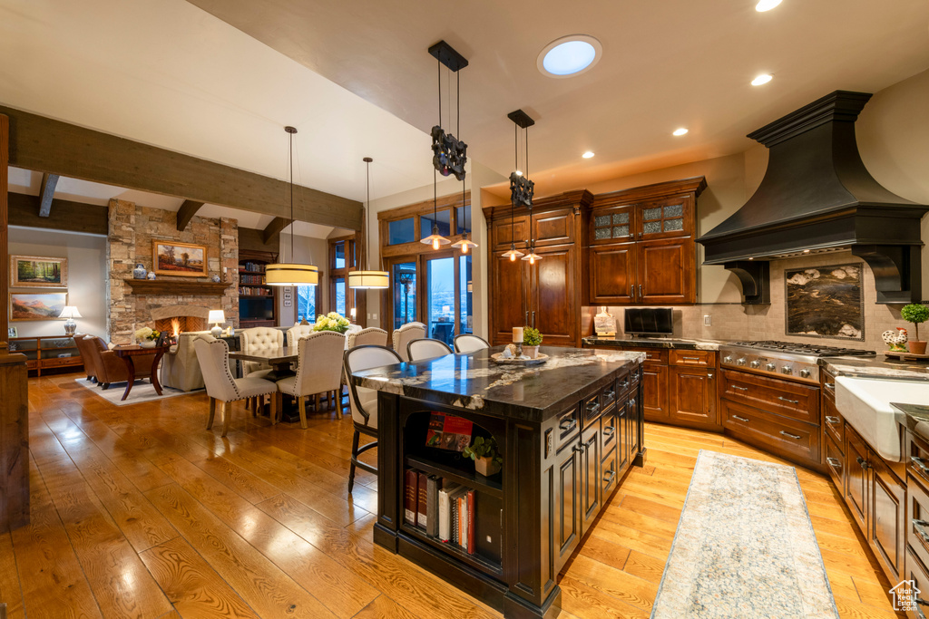 Kitchen with light wood-type flooring, a fireplace, a center island, dark stone counters, and premium range hood