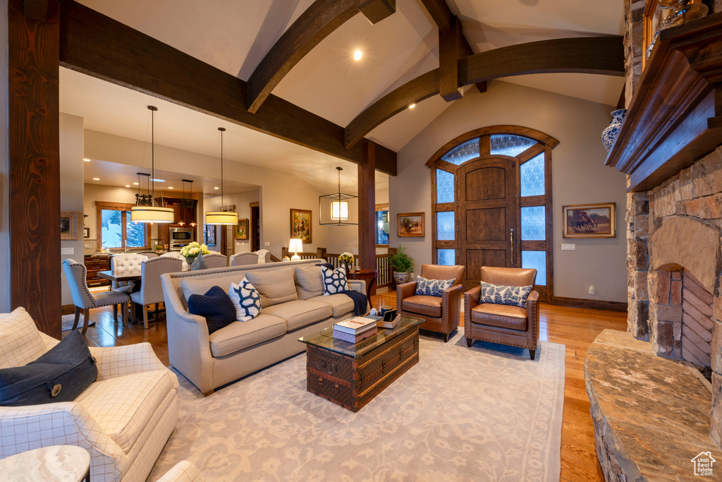 Living room with light wood-type flooring, beamed ceiling, high vaulted ceiling, and a stone fireplace