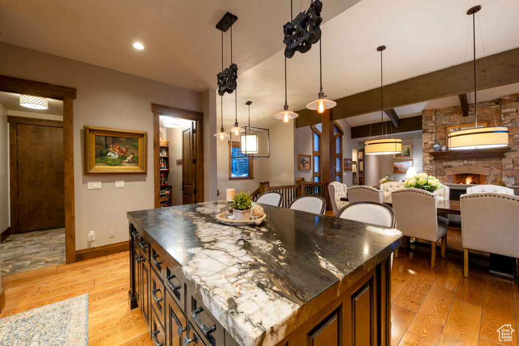 Kitchen featuring light hardwood / wood-style flooring, lofted ceiling with beams, a center island, dark stone countertops, and a stone fireplace