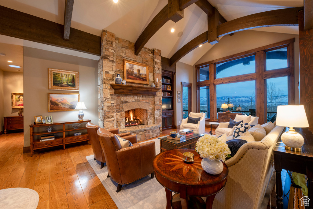 Living room featuring a stone fireplace, light hardwood / wood-style flooring, beamed ceiling, and a mountain view