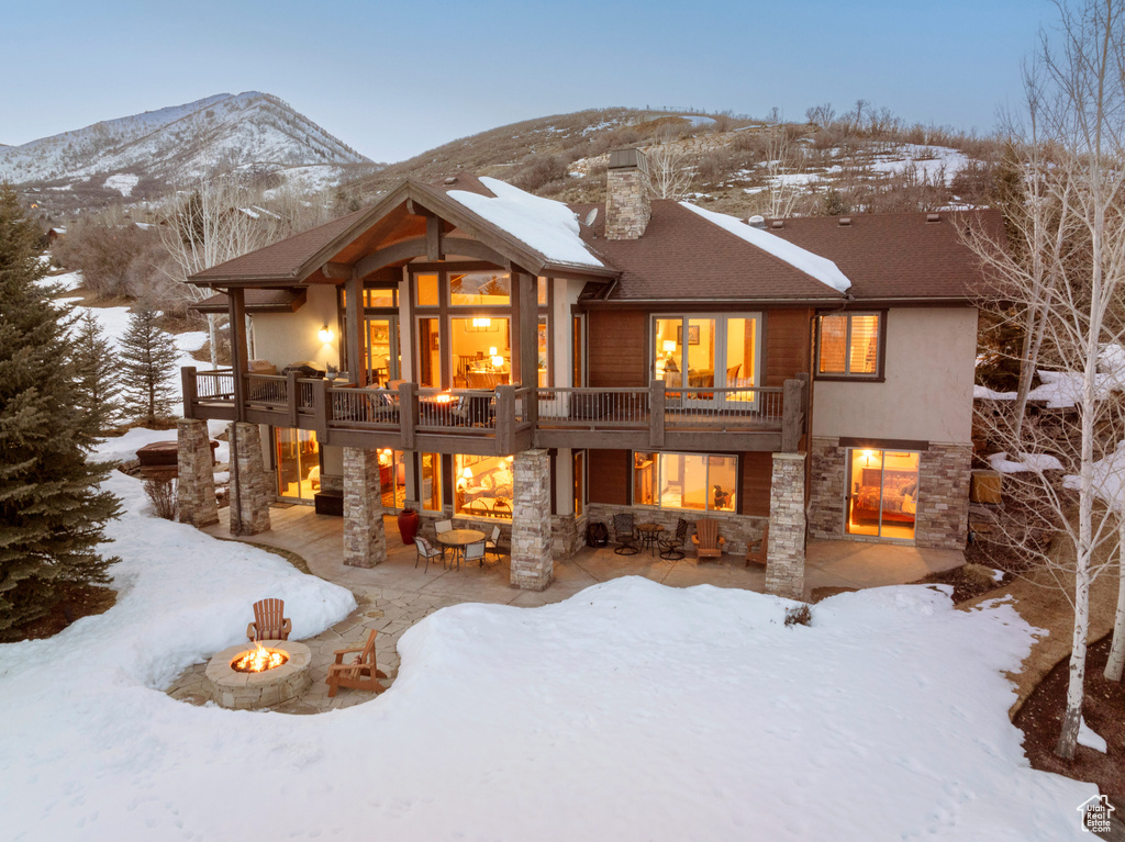 Snow covered house featuring a mountain view, a balcony, an outdoor fire pit, and a patio area