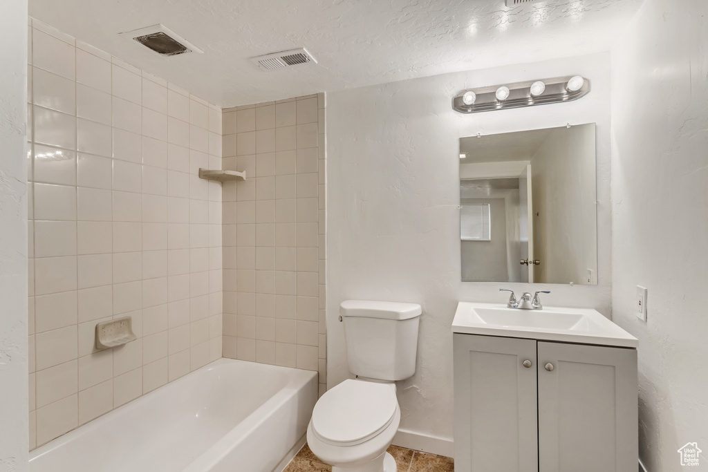 Full bathroom with tiled shower / bath, oversized vanity, a textured ceiling, toilet, and tile flooring