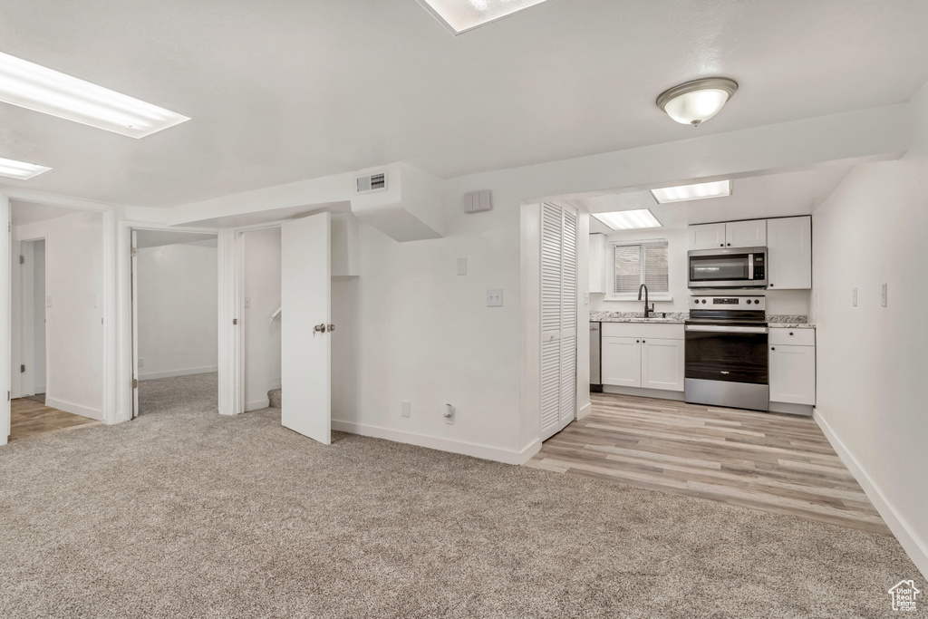 Kitchen with sink, appliances with stainless steel finishes, light colored carpet, and white cabinetry